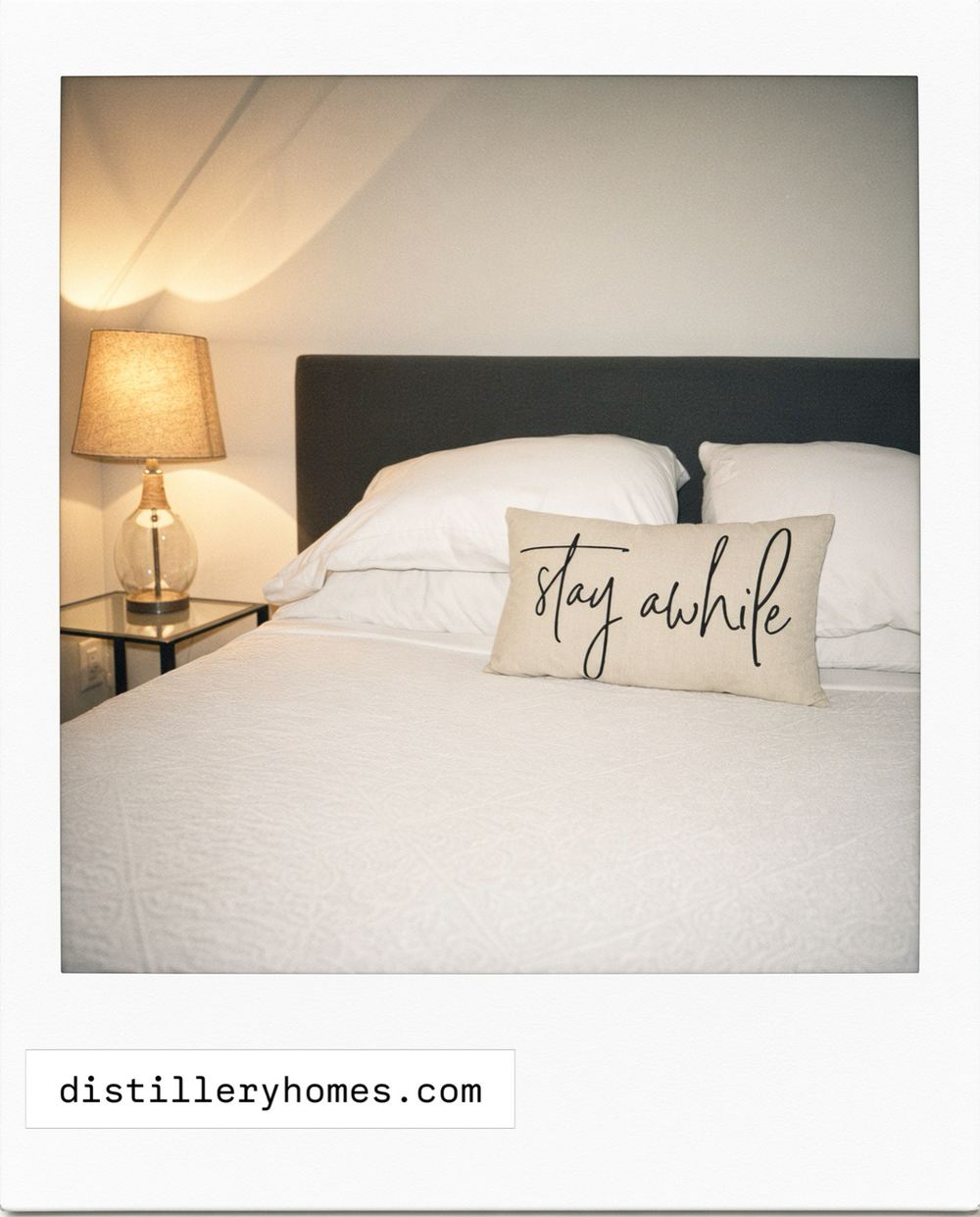 Queen bed with white linens, charcoal upholstered headboard and a glass bedside lamp at 763 Monmouth Road